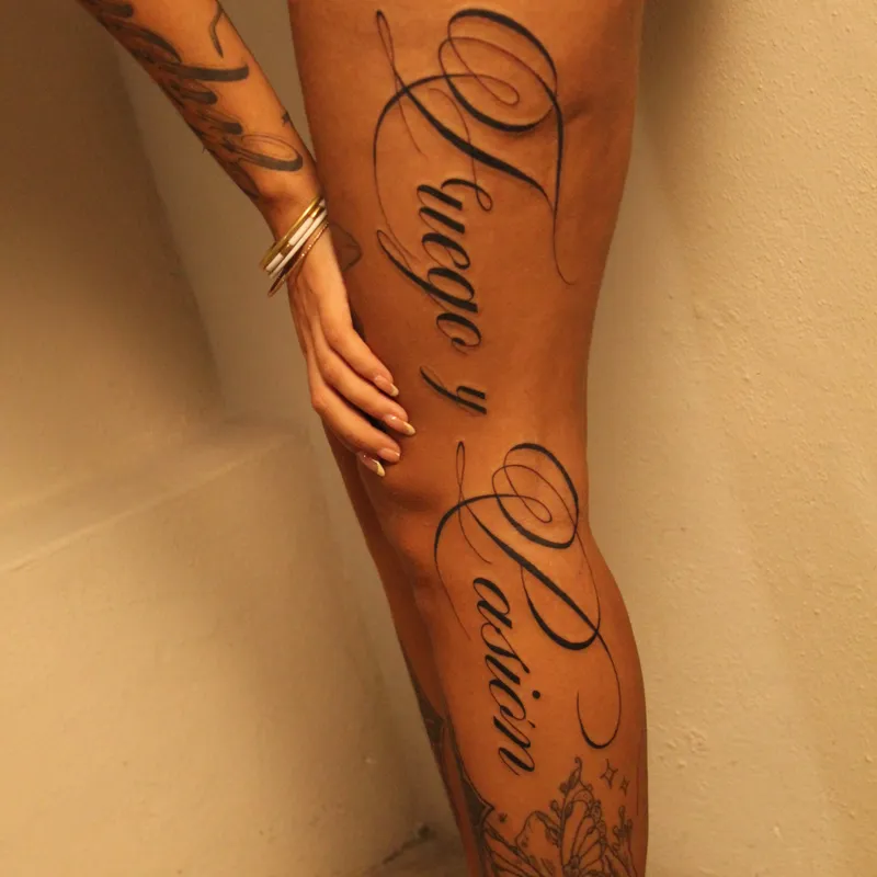 Fuego y Pasión elegant script calligraphy tattoo on thigh